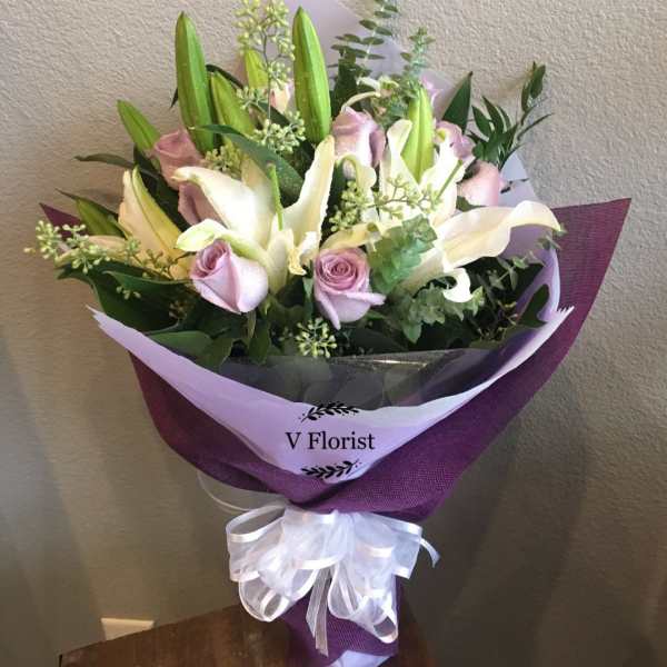 Bouquet of white lilies and pale pink roses wrapped in purple paper