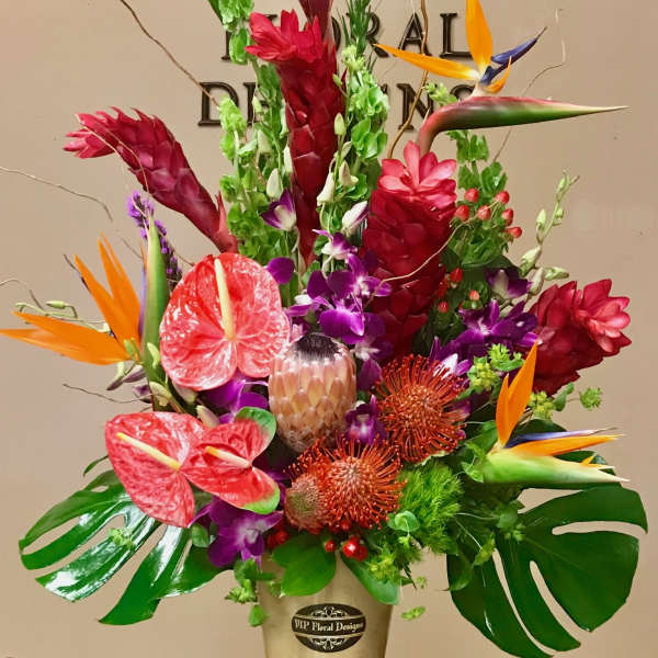 Tall tropical arrangement with red, orange, and purple flowers in a pedestal vase