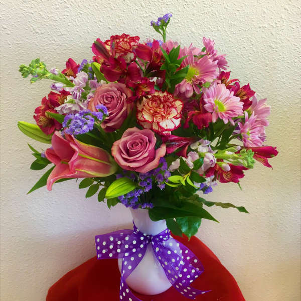Mixed bouquet of pink and purple flowers in a white vase with a purple ribbon