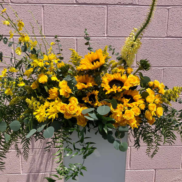 Yellow sunflowers and roses arranged in a tall white vase
