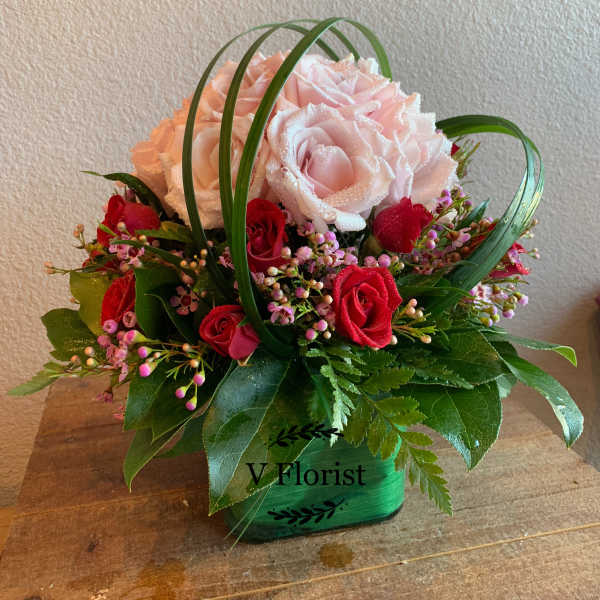 Short arrangement of pink and red roses with looping grass in a green cube vase