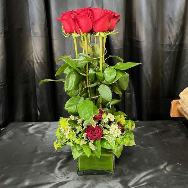 Tall arrangement of red roses in a glass vase with a low cluster of mixed flowers