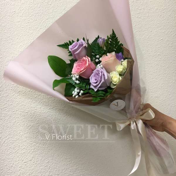 Pastel bouquet of pink and lavender roses wrapped in pink paper with a satin ribbon bow