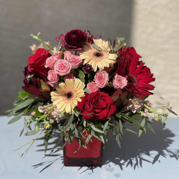 Red and pink rose bouquet with gerbera daisies in a red vase