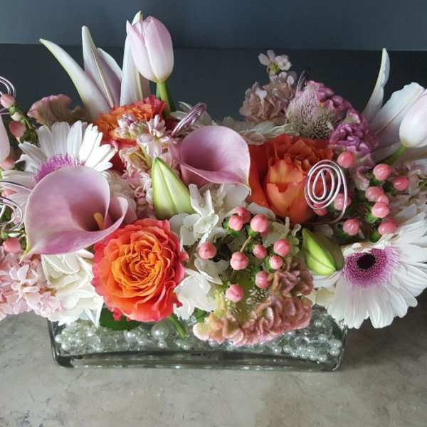 Pink and white floral arrangement with orange roses in a glass vase