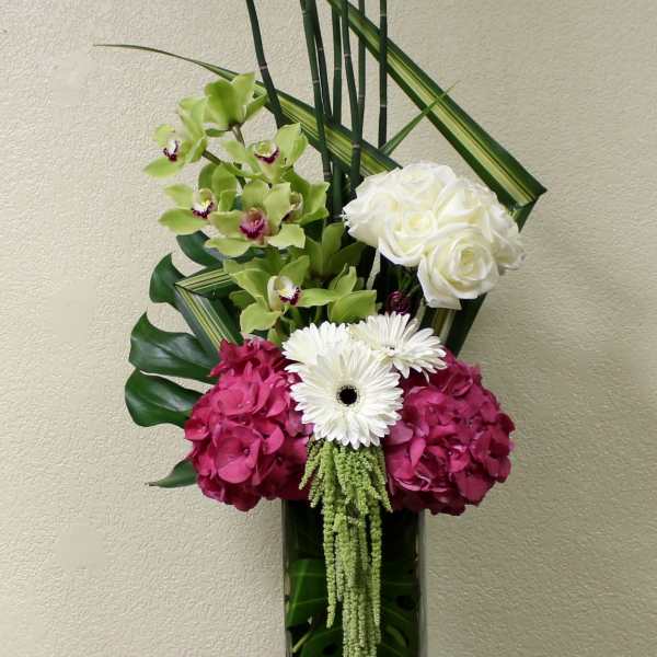 Tall floral arrangement in a glass vase with white roses, orchids, and pink hydrangeas