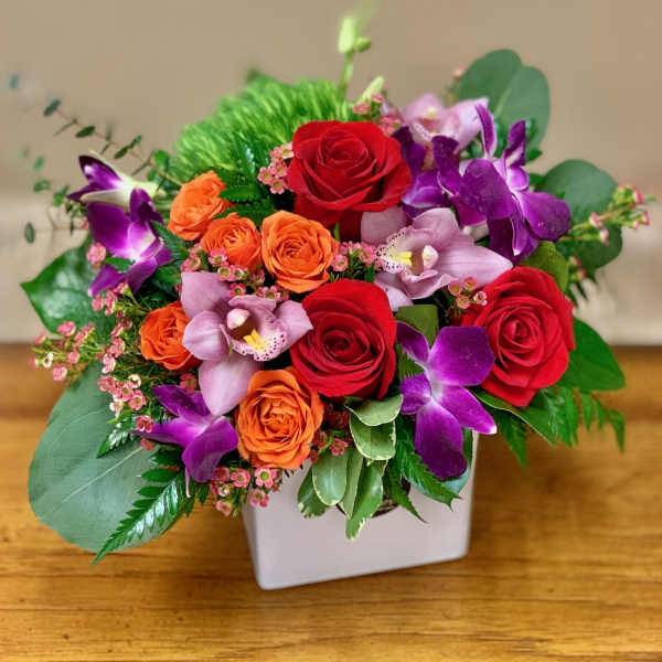 Bouquet of red and orange roses with purple orchids in a white vase
