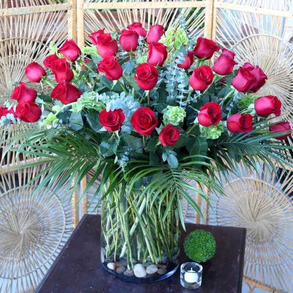 Red roses arranged in a clear glass vase with greenery and palm fronds