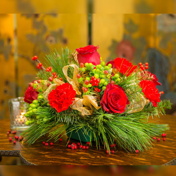 Red roses and carnations in a low holiday arrangement with pine and berries