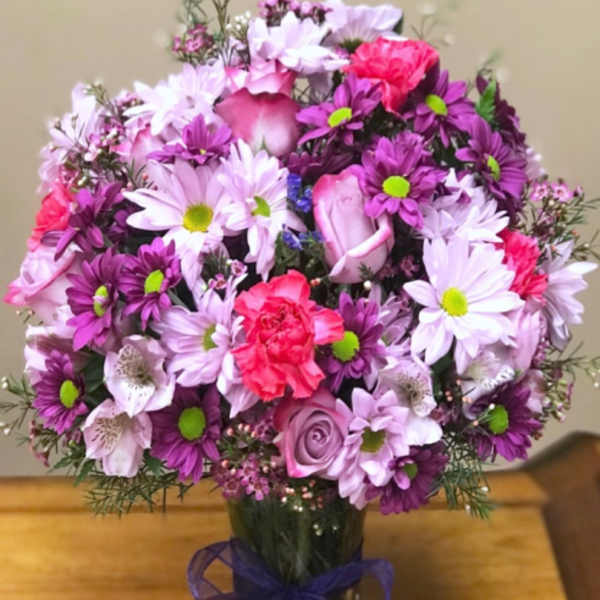Bouquet of pink and purple flowers in a glass vase with a ribbon