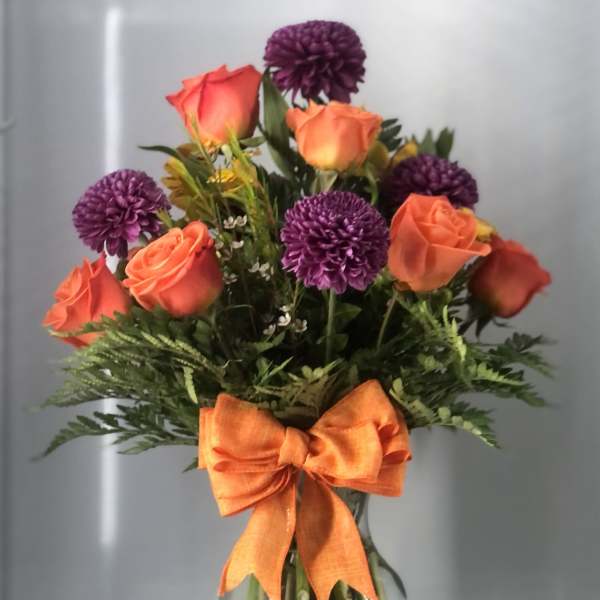 Bouquet of orange roses and purple pompon flowers in a glass vase with an orange bow