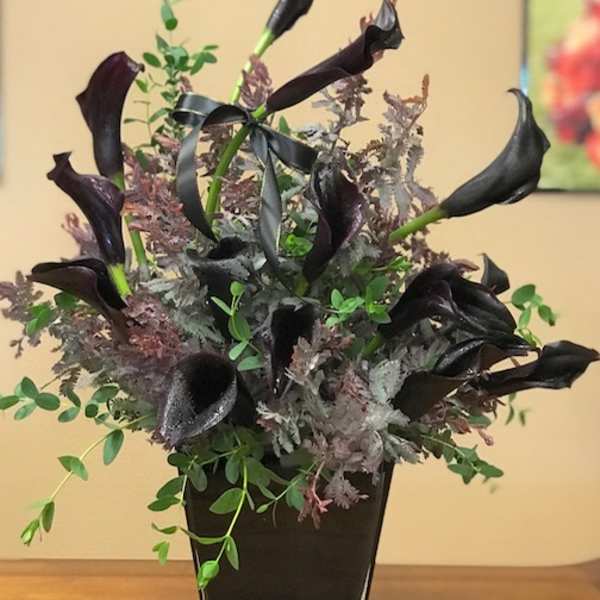 Black calla lilies in a square black vase with mixed greenery