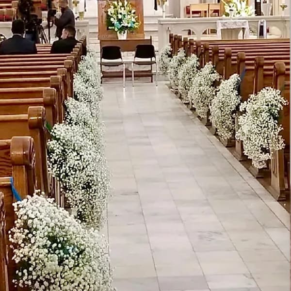 White floral arrangements line the aisle of a church interior.