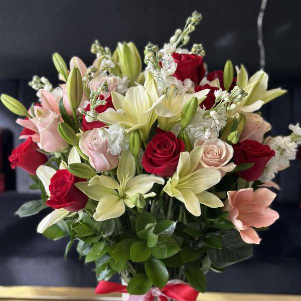 Bouquet of red and blush roses with pale lilies in a glass vase