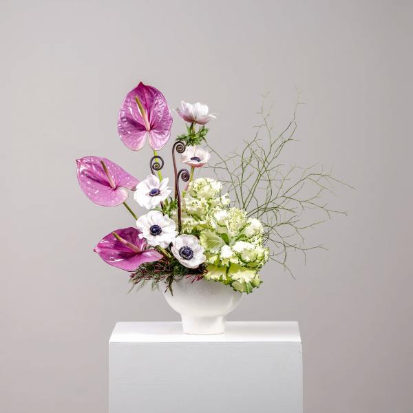 Modern arrangement with pink heart-shaped blooms, white anemones, and green ruffled flowers in a white bowl vase