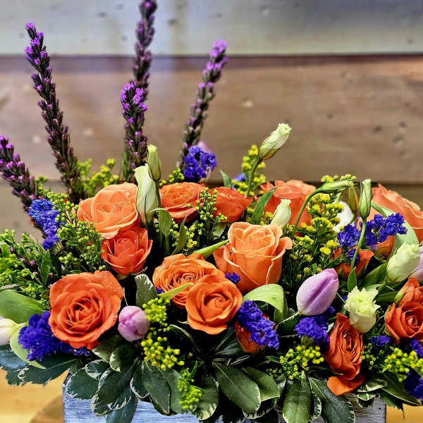 Orange roses and purple flowers in a low rectangular arrangement