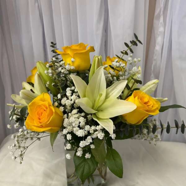 Yellow roses and white lilies in a clear glass vase