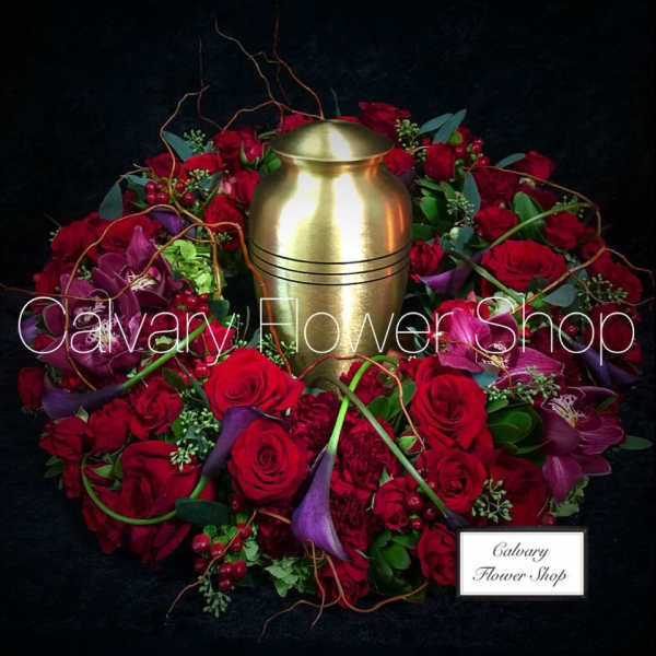 Red rose and orchid wreath around a gold urn on a black background
