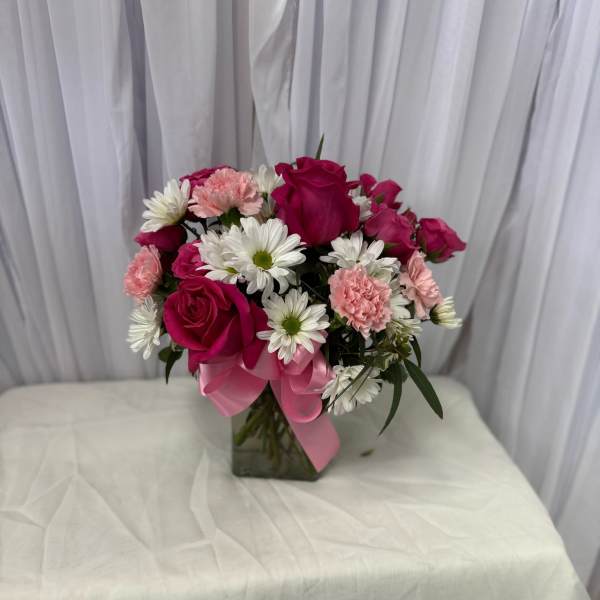 Pink roses and white daisies arranged in a glass vase with a pink ribbon