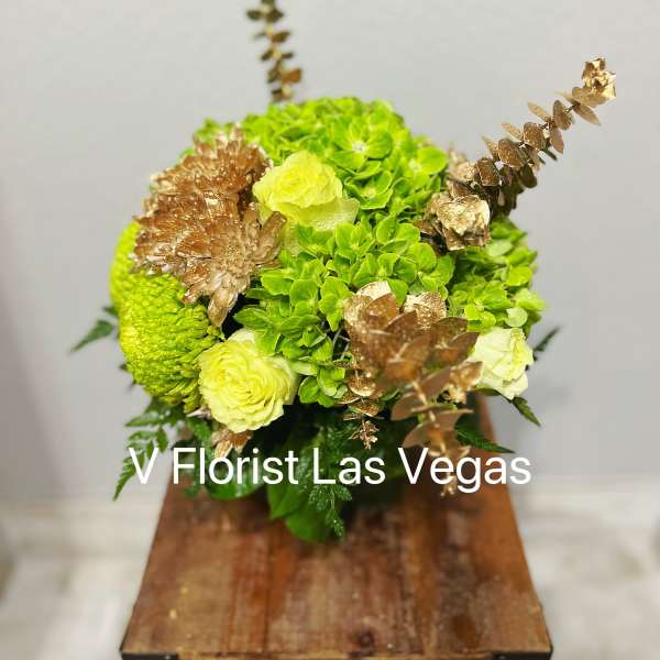 Green and pale yellow floral arrangement with gold accents in a wooden container