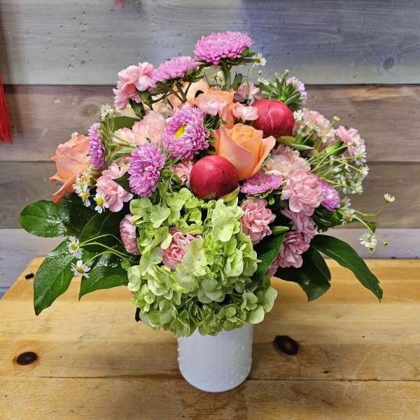 Pink and peach bouquet in a white vase with green hydrangea and red ornaments