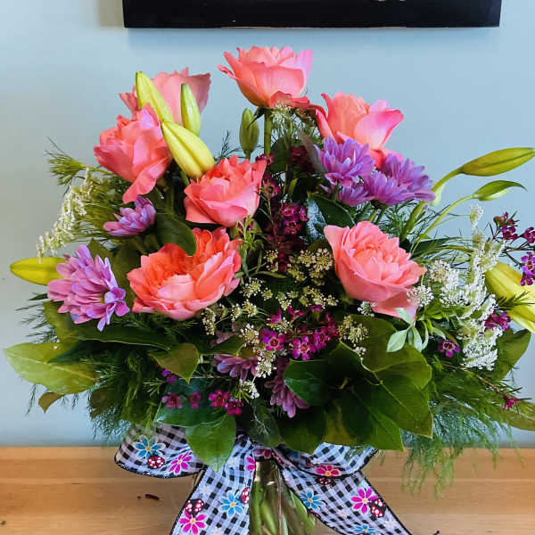 Pink roses and purple daisies in a glass vase with a patterned bow