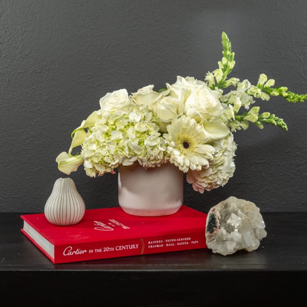 White floral arrangement in a small vase with calla lilies and roses