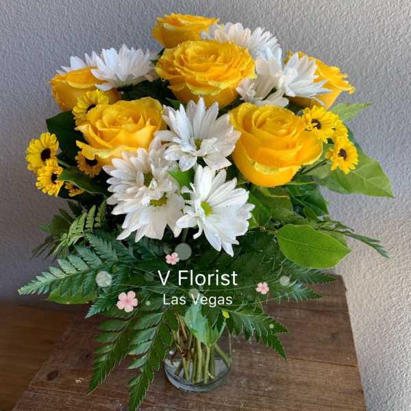 Arrangement of yellow roses and white daisies in a clear glass vase on a wooden surface