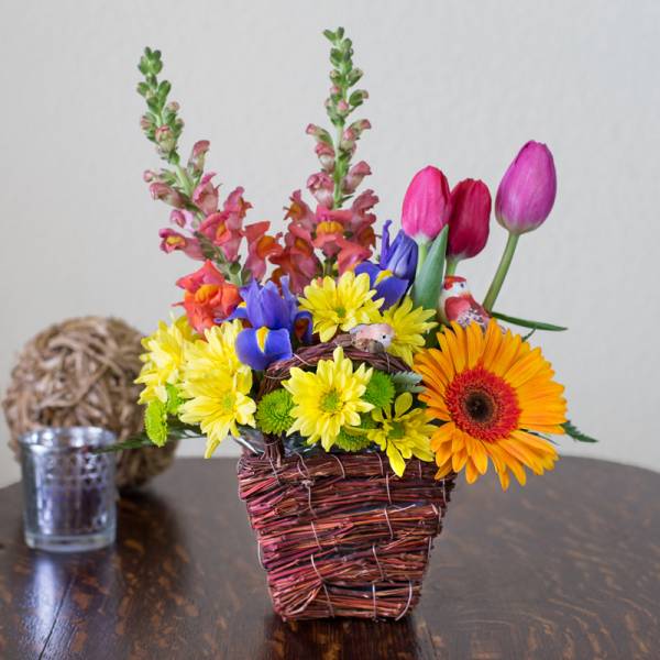 Colorful mixed flower arrangement in a woven basket with tulips and daisies