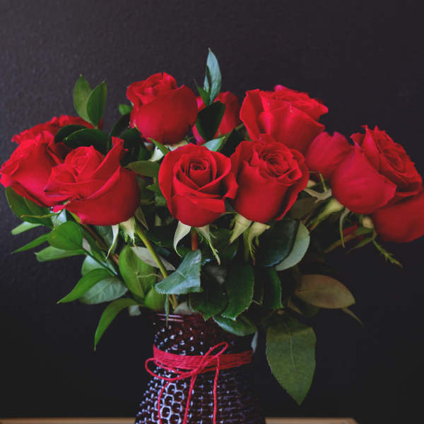 Red roses arranged in a textured vase with a red cord and heart charm