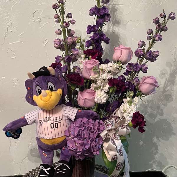 Purple floral arrangement with a Rockies mascot plush in a vase