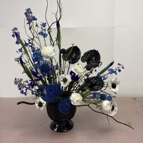 Blue and white floral arrangement in a black vase with tall curly branches