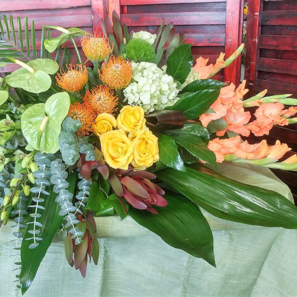 Tropical floral arrangement with yellow roses, orange blooms, and peach gladiolus