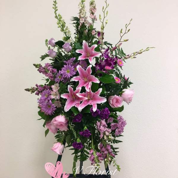 Tall floral standing spray with pink lilies and purple blooms on an easel