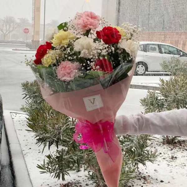 Handheld bouquet of red, pink, and white carnations wrapped in pink paper with a bow