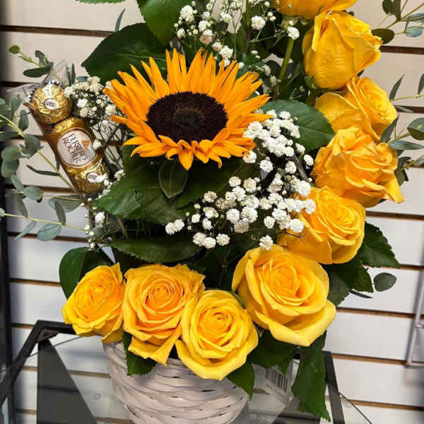 Yellow roses and a sunflower in a white basket with chocolates