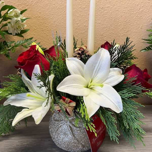 Holiday floral centerpiece with white lilies, red roses, and two taper candles