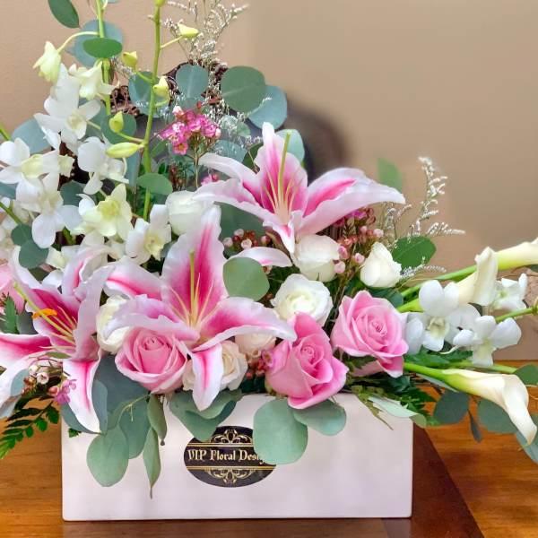 Pink lilies and roses arranged in a white box with white orchids