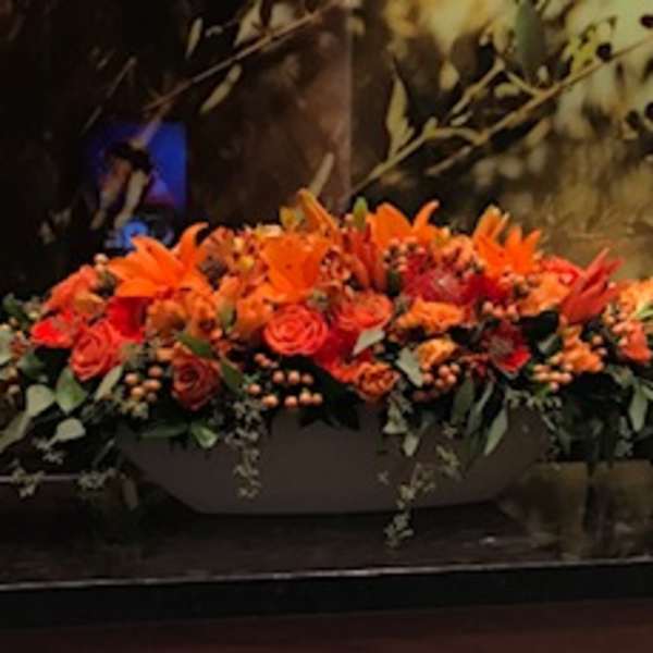 Long orange floral arrangement with roses and lilies in a low container