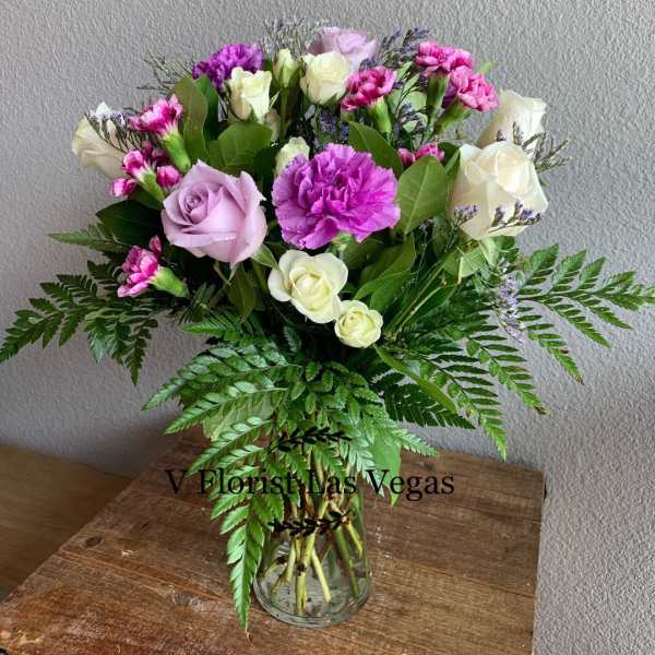 Mixed bouquet of lavender roses, white roses, and purple carnations in a clear glass vase