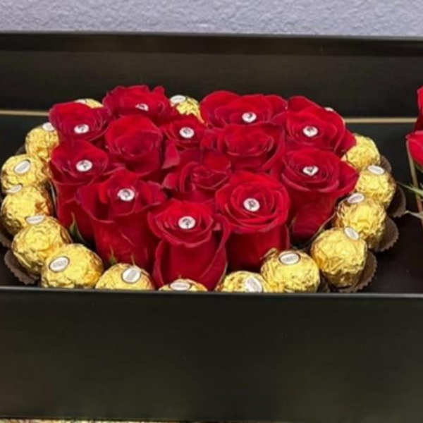 Red roses arranged in a black presentation box with gold-wrapped chocolates