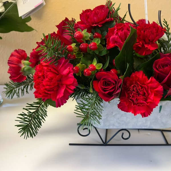 Red carnations and roses arranged in a sleigh-shaped container