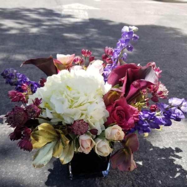 Bouquet of white hydrangea, roses, and purple flowers in a black vase