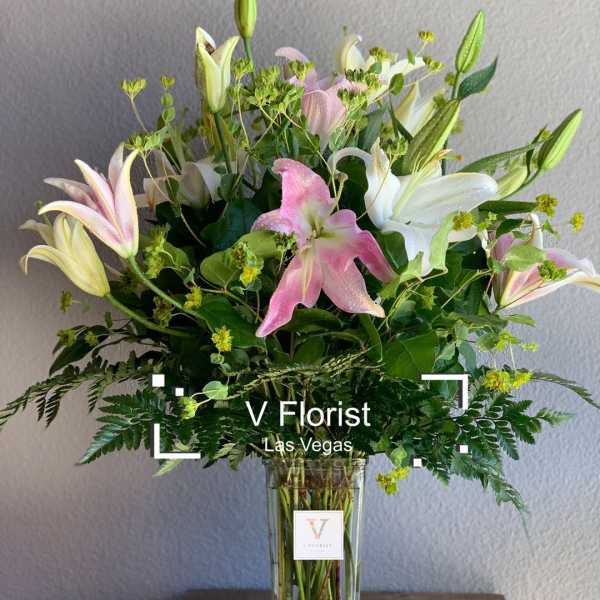 Tall arrangement of pink and white lilies with buds in a clear glass vase with ferns.