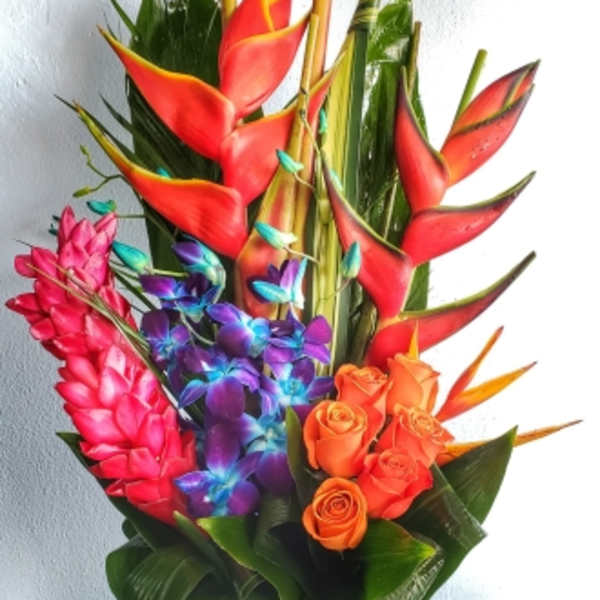 Tropical bouquet with red heliconia, orange roses, and purple orchids in a white vase