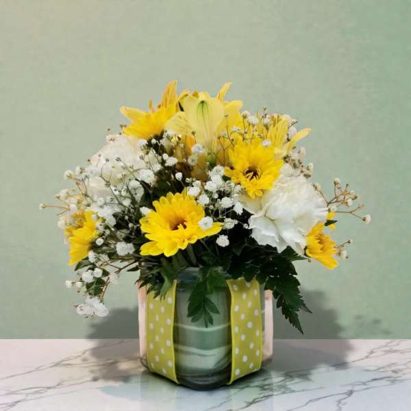 Yellow and white flower arrangement in a glass vase with a polka-dot ribbon