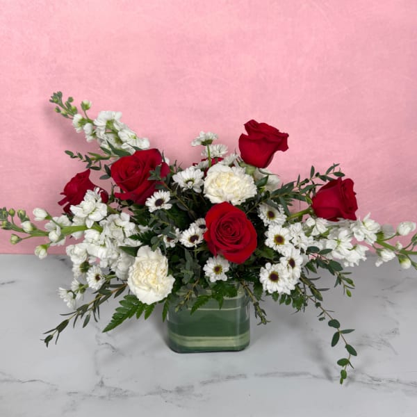 Red roses and white flowers arranged in a square glass vase