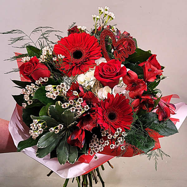 Hand-tied bouquet of red roses and gerbera daisies with white accents and a red heart pick