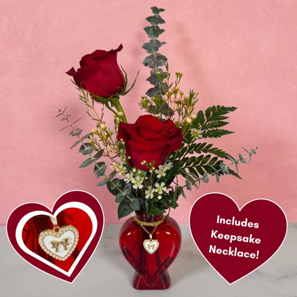 Two red roses in a red heart-shaped vase with a necklace pendant