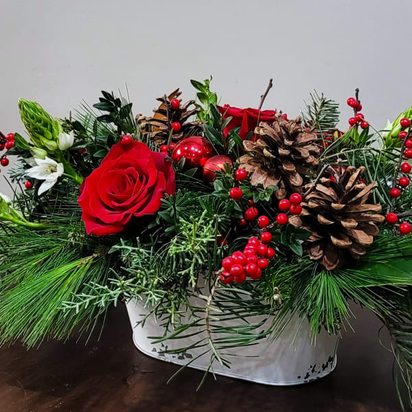 Low Christmas centerpiece with red roses, red berries, pinecones, and evergreen in a white container